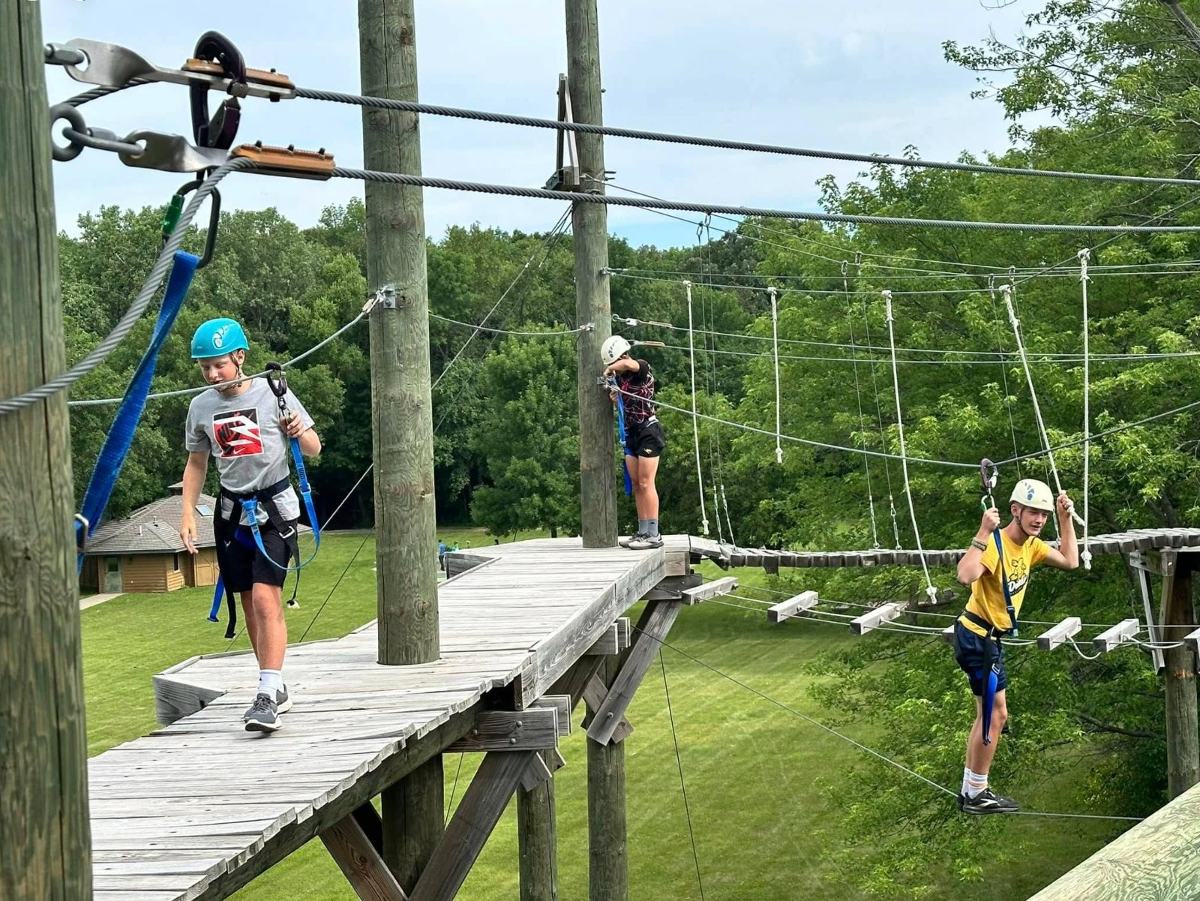 Camp Perthes kids on a high ropes course in helmets and harnesses, cheering each other on