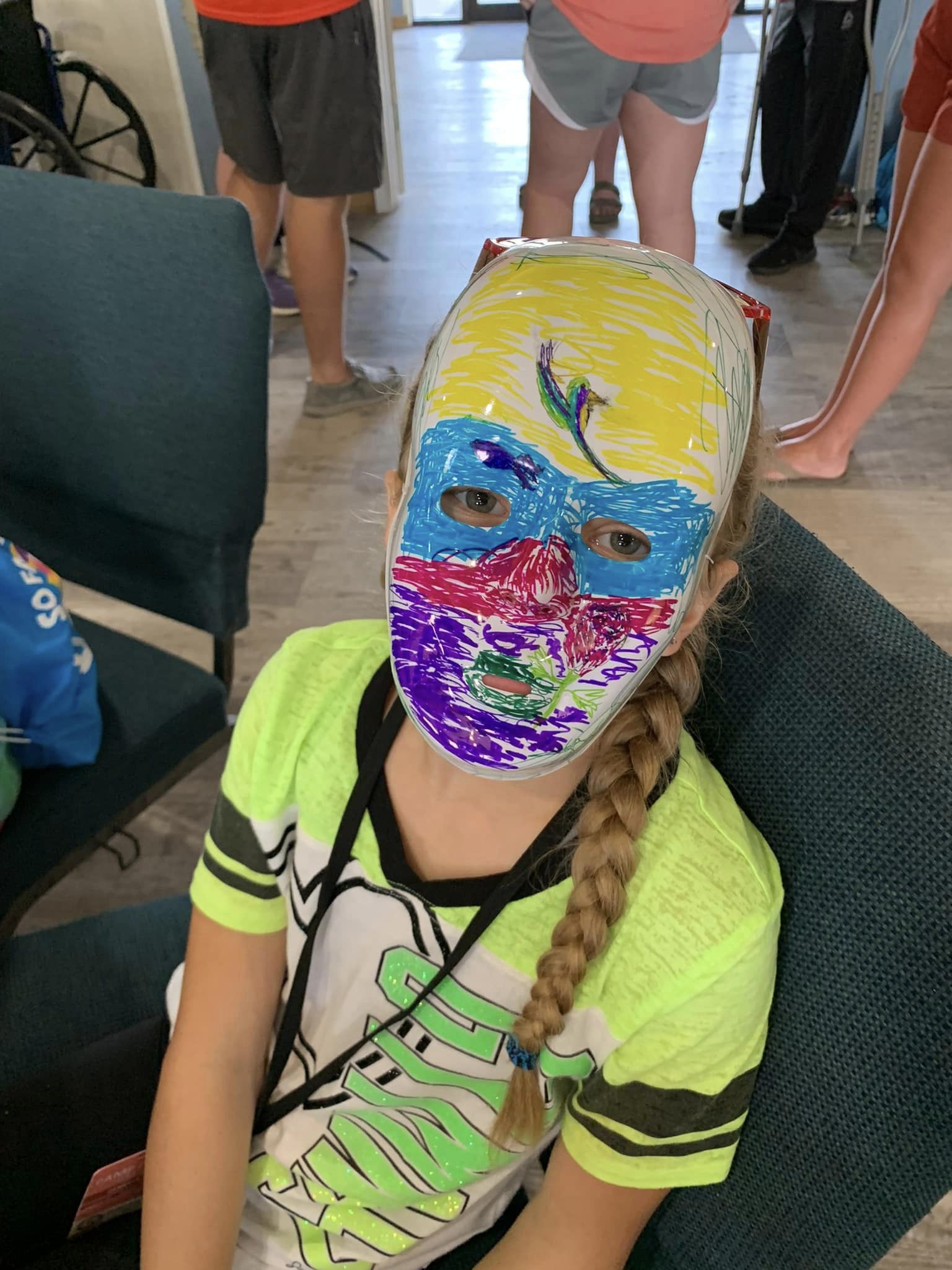 A girl wearing a plaster face mask she painted in yellow, blue, pink and purple