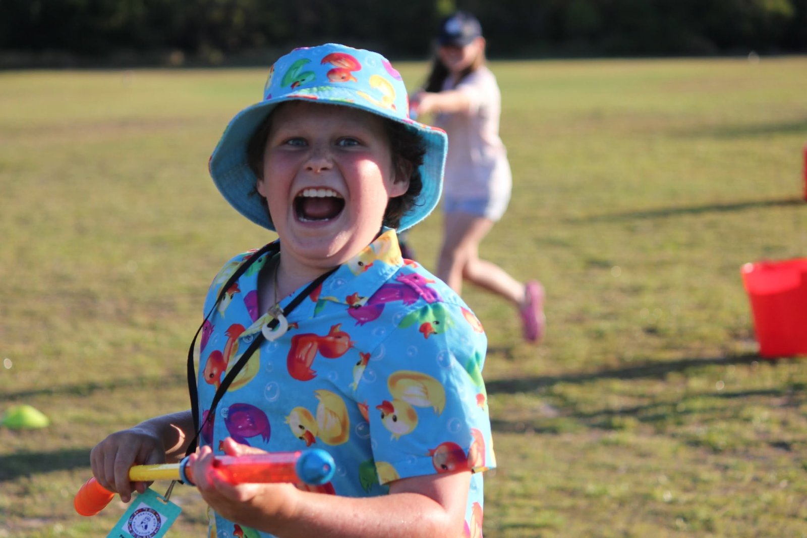 A boy in a bucket hat laughing with pure delight during a camp water game