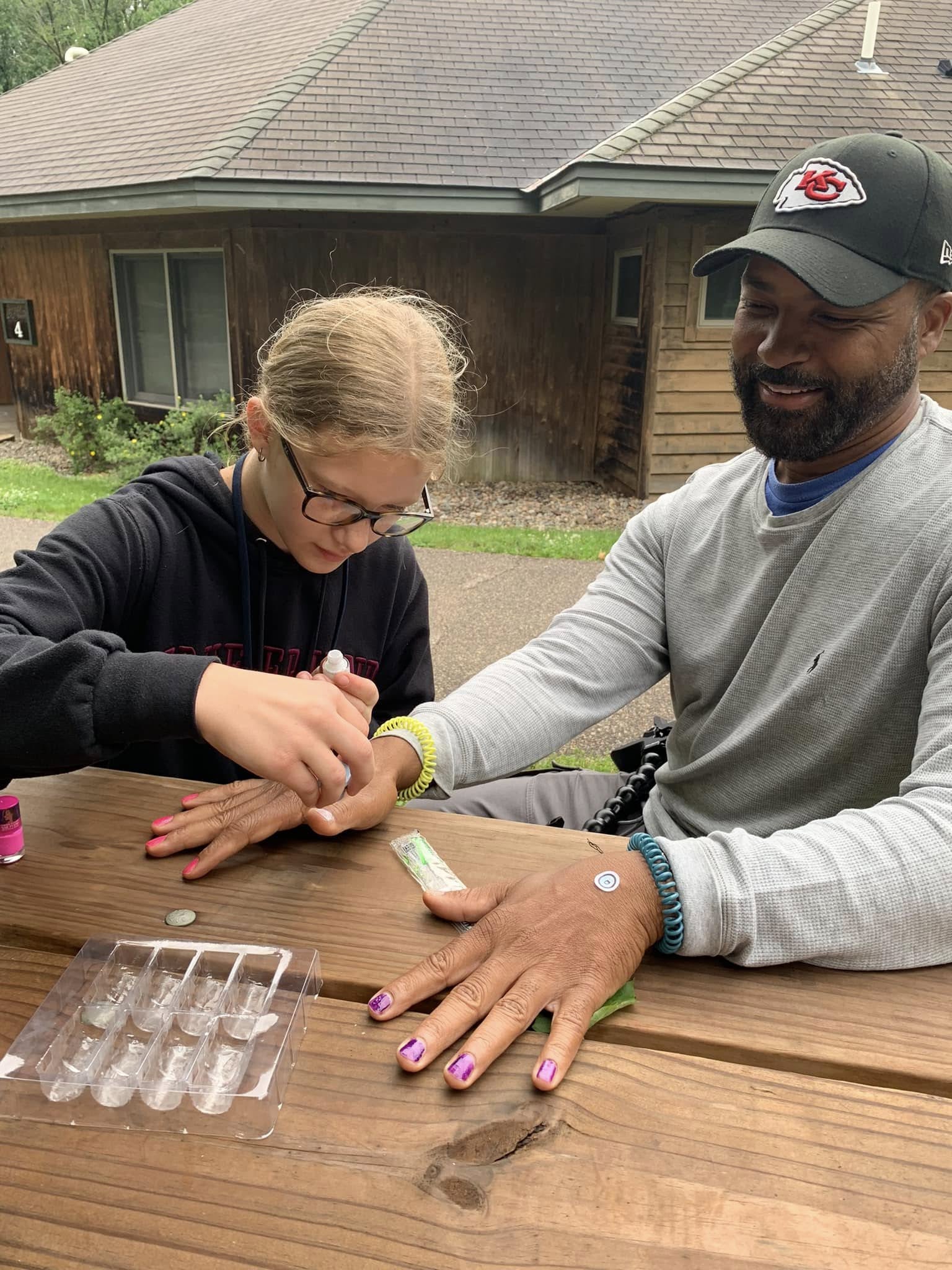 A volunteer laughing as a camper paints his nails at camp